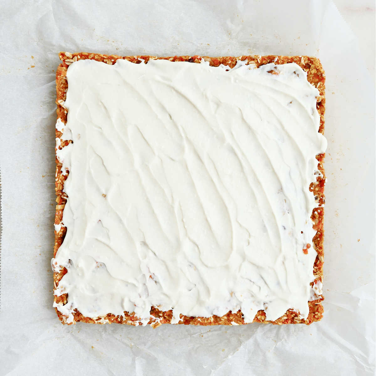 Healthy no bake carrot cake bars topped with frosting before slicing on parchment paper.