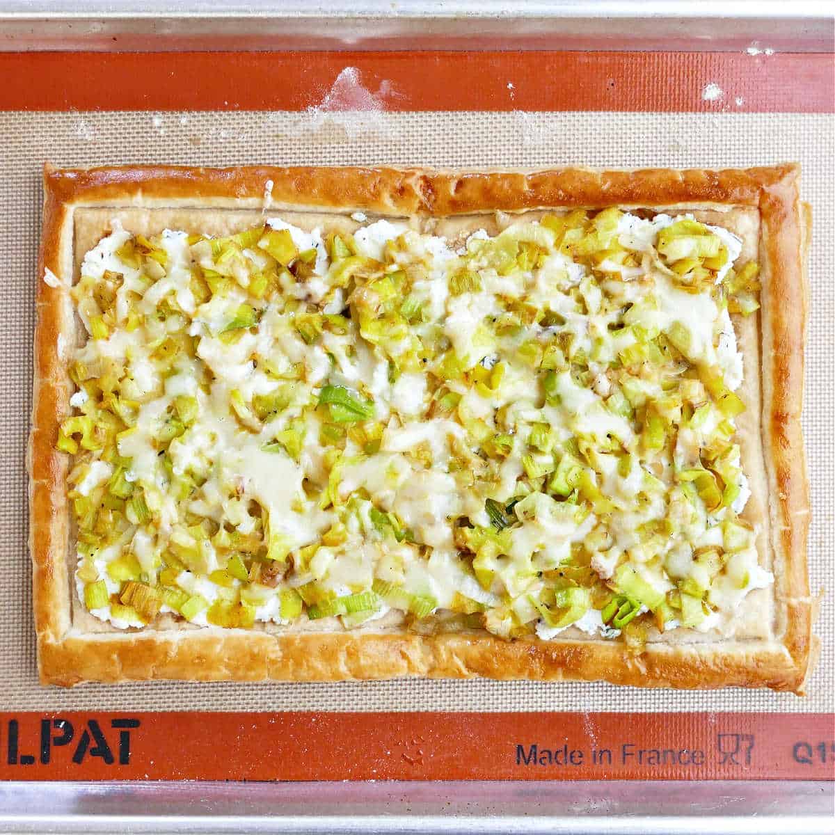 Leek and cheese tart on a baking sheet after cooking.