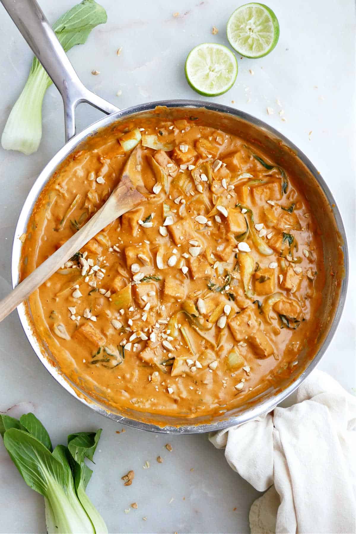 Peanut butter tofu made with coconut milk in a large skillet with wooden spoon.