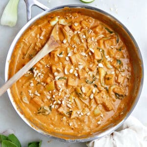 Coconut milk tofu in a peanut butter sauce in a large pan with a wooden spoon.
