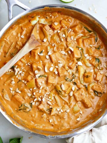 Coconut milk tofu in a peanut butter sauce in a large pan with a wooden spoon.