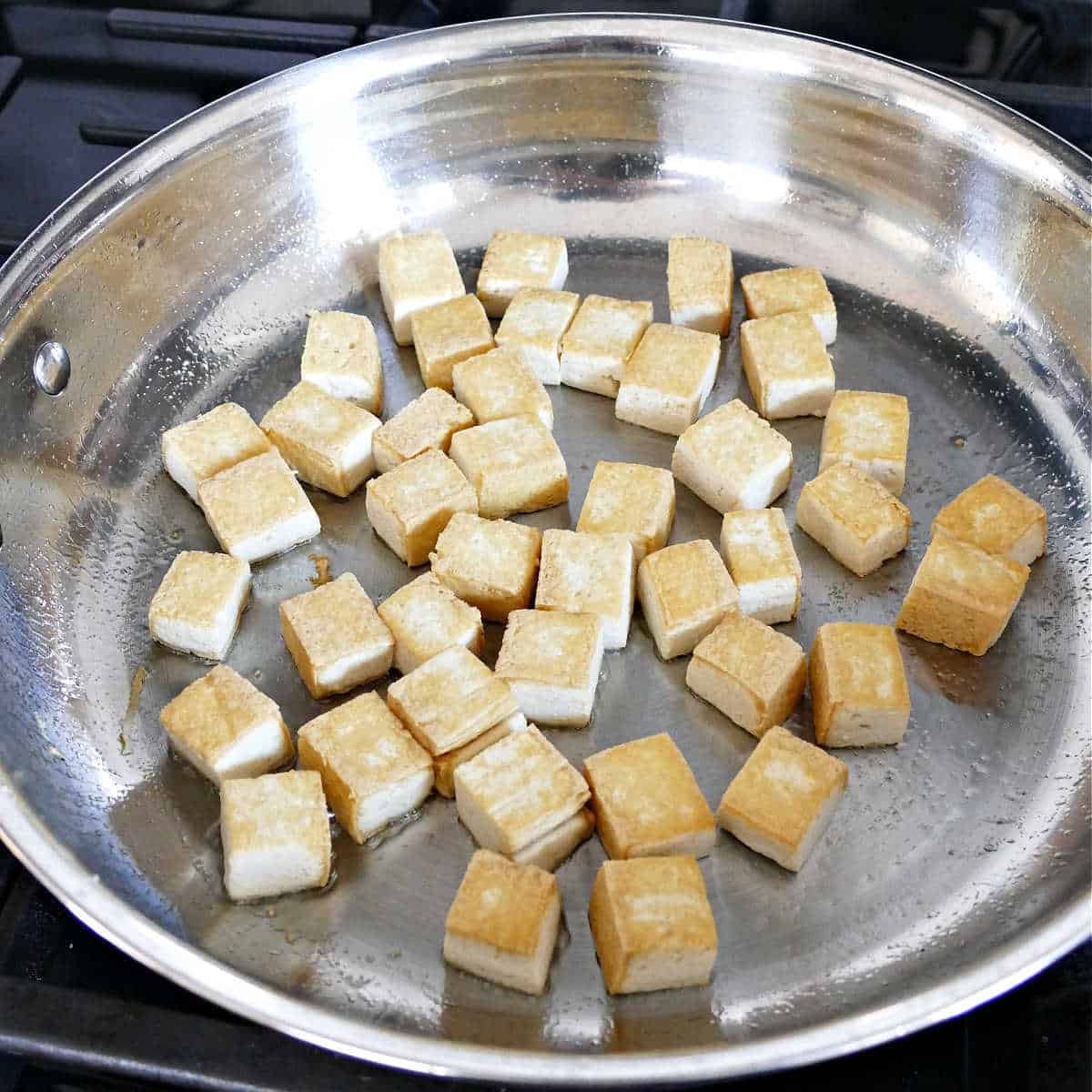 Searing the diced tofu in a large skillet.