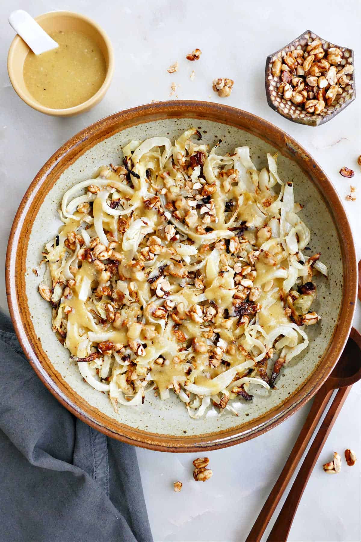 Roasted cabbage salad in a large bowl next to a ramekin of nuts and dressing.