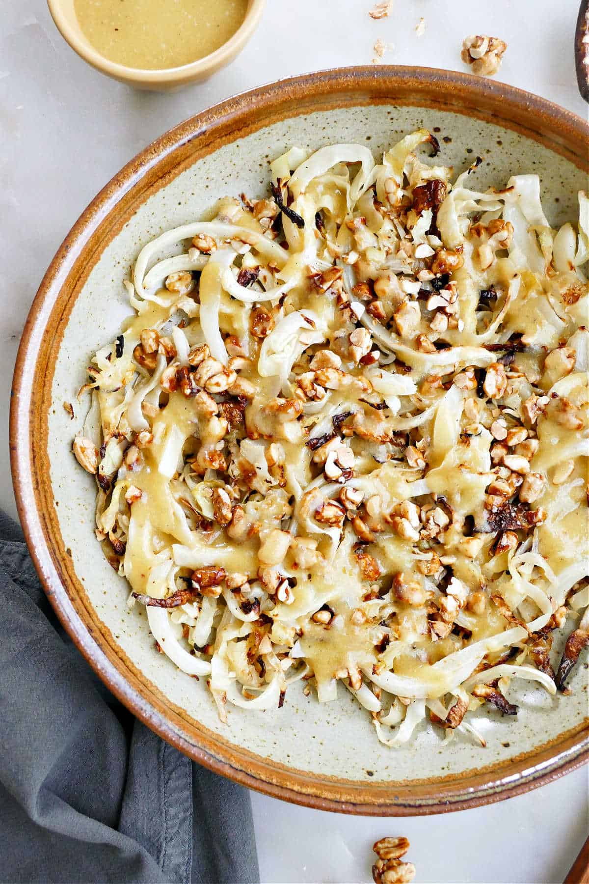 Roasted cabbage salad in a large tan and brown bowl next to dressing.