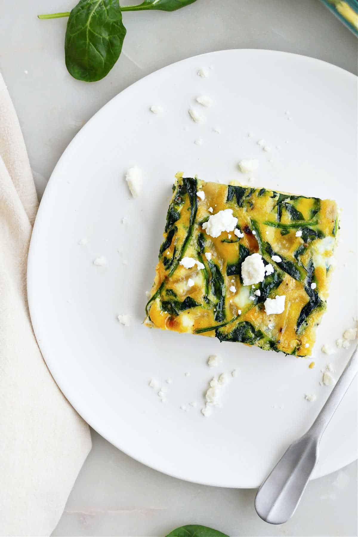 A square of spinach feta egg bake on a plate topped with more feta cheese.