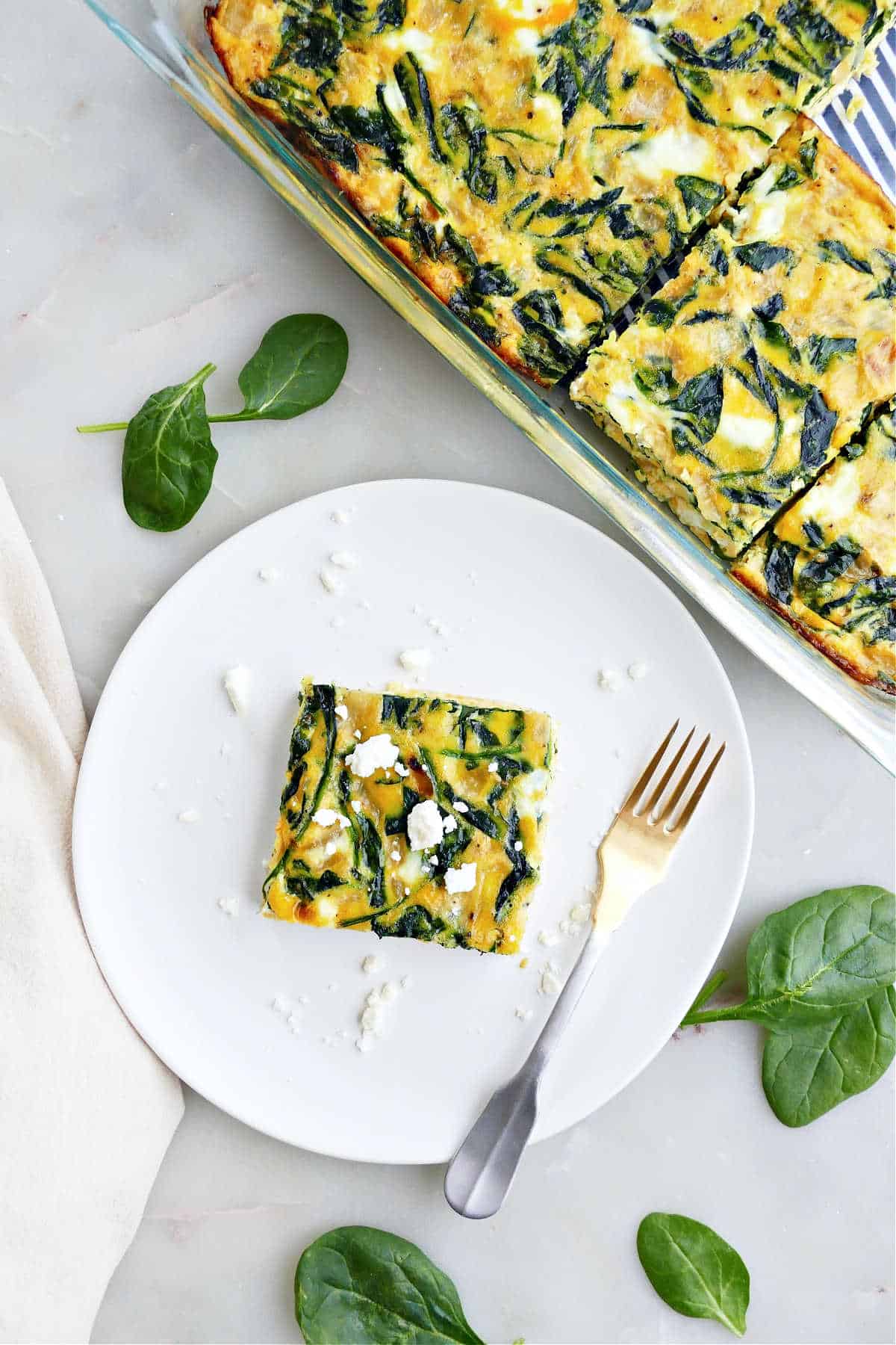 Spinach feta egg bake in a dish, next to a serving on a plate with a fork.