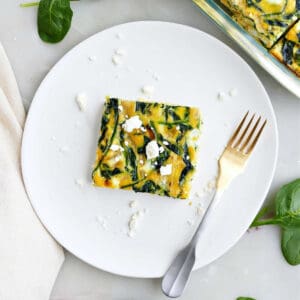 A serving of spinach feta egg bake on a white plate next to spinach leaves.