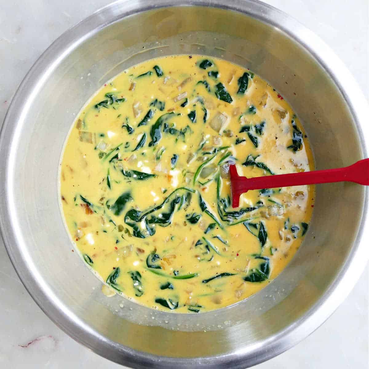 Whisked eggs in a mixing bowl with spinach.