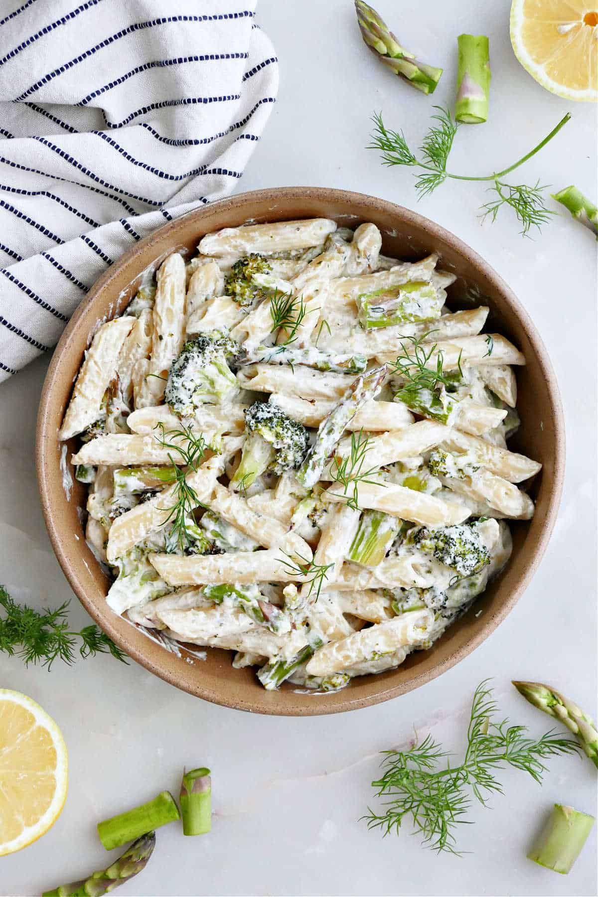 A large bowl of asparagus broccoli pasta garnished with herbs next to a striped dish towel.