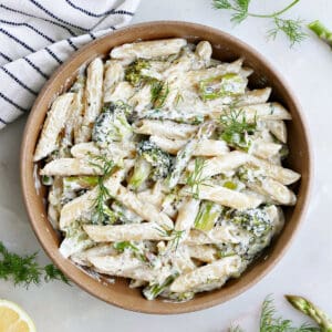 Asparagus broccoli pasta garnished with herbs next to a lemon and striped dish towel.