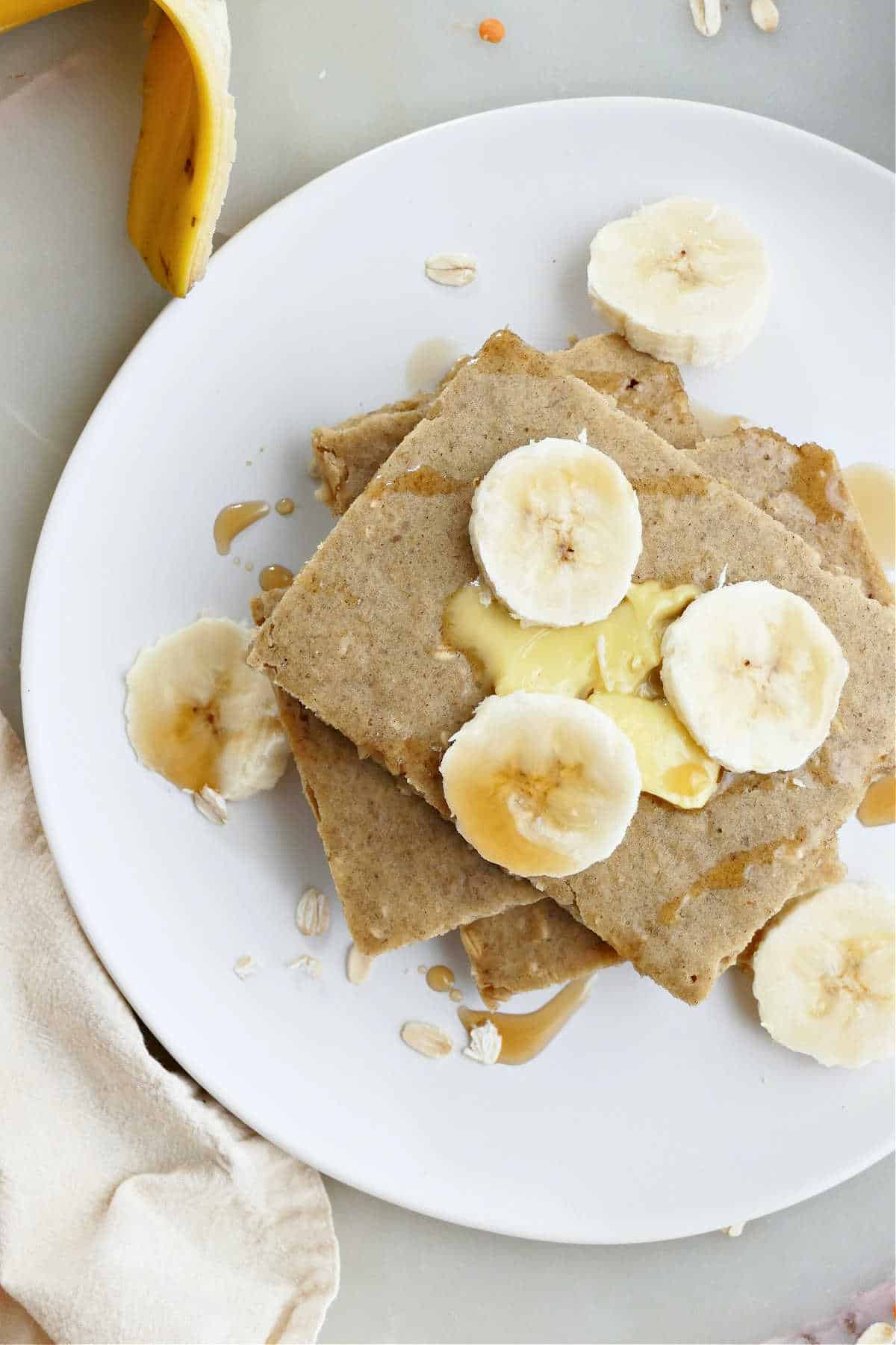 Baked banana pancakes sliced into squares on a white plate with sliced bananas.