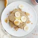 Baked banana pancakes topped with freshly sliced bananas on a white plate.