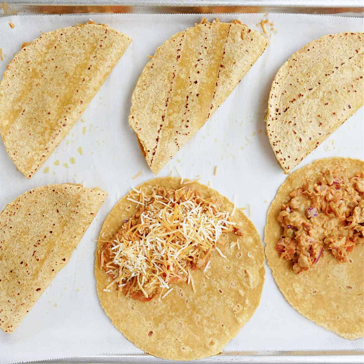 Tortillas on a baking sheet, assembling the buffalo chickpea tacos.