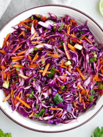 Cabbage carrot slaw in a large serving bowl next to a lime.