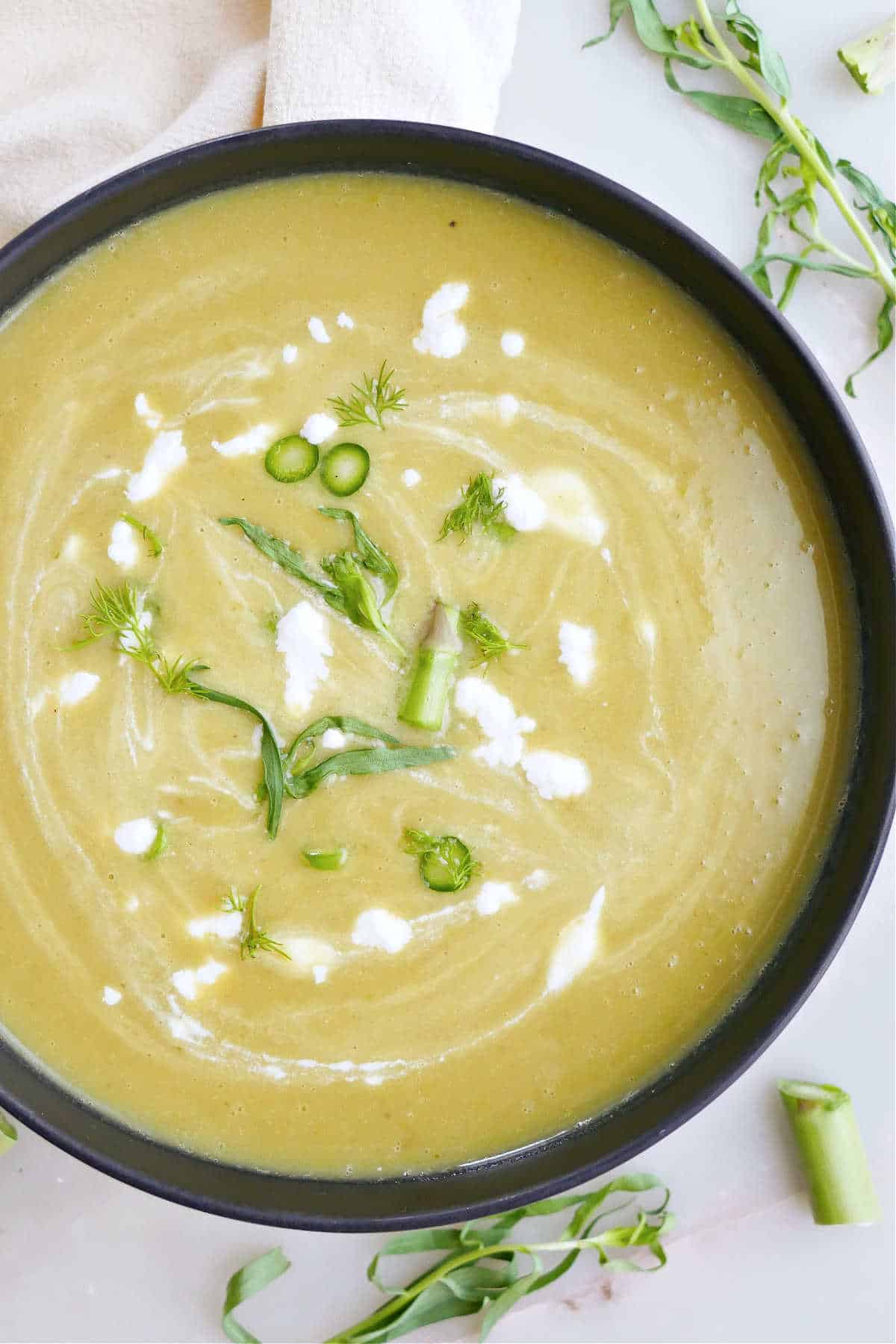 Cold asparagus soup garnished with herbs and asparagus.