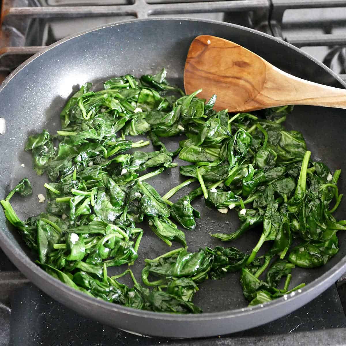 Spinach cooking in a skillet on a stove with a spoon.
