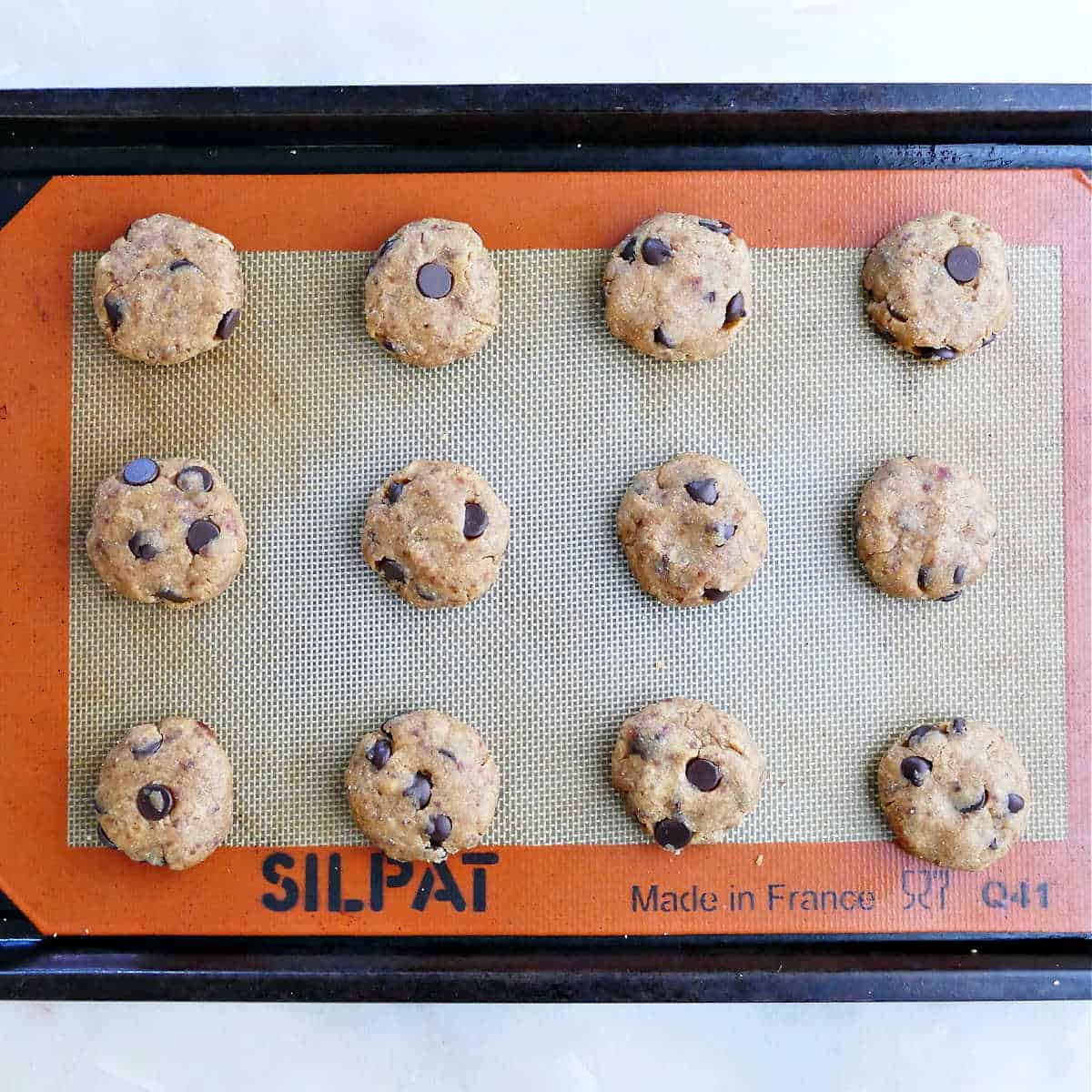 Sweetened date cookies with chocolate chips on a cookie sheet before baking.