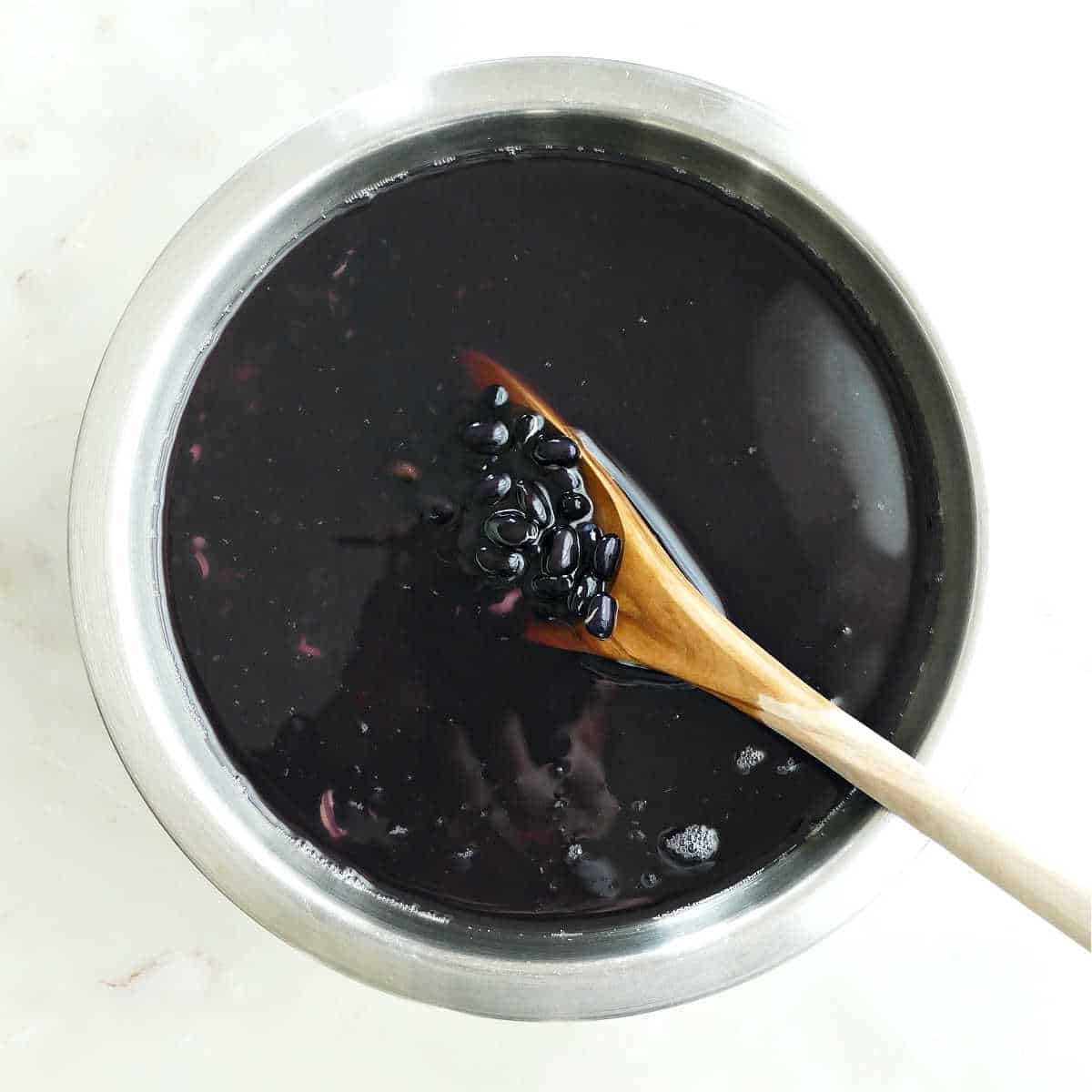 A large bowl of dried black beans with a wooden spoon.