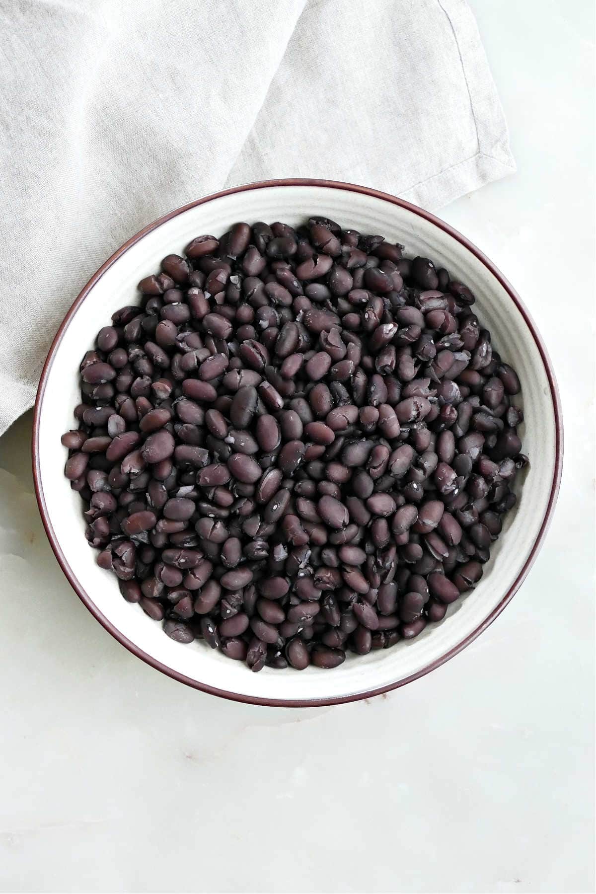 A large serving bowl of cooked black beans next to a white kitchen towel.
