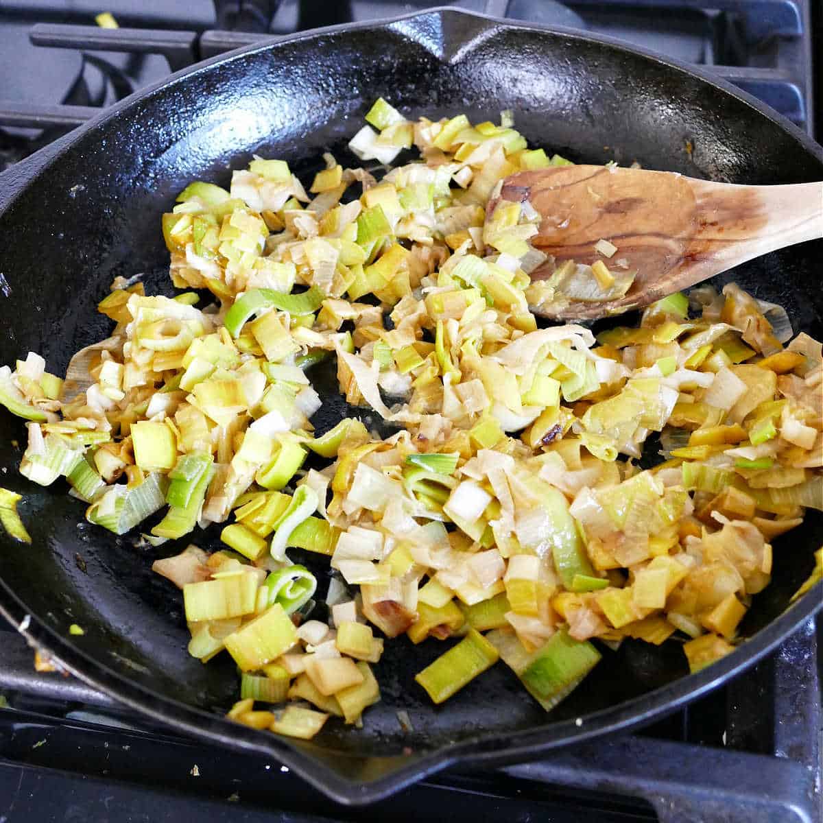 Cooking leeks in a large skillet, stirring with a wooden spoon.