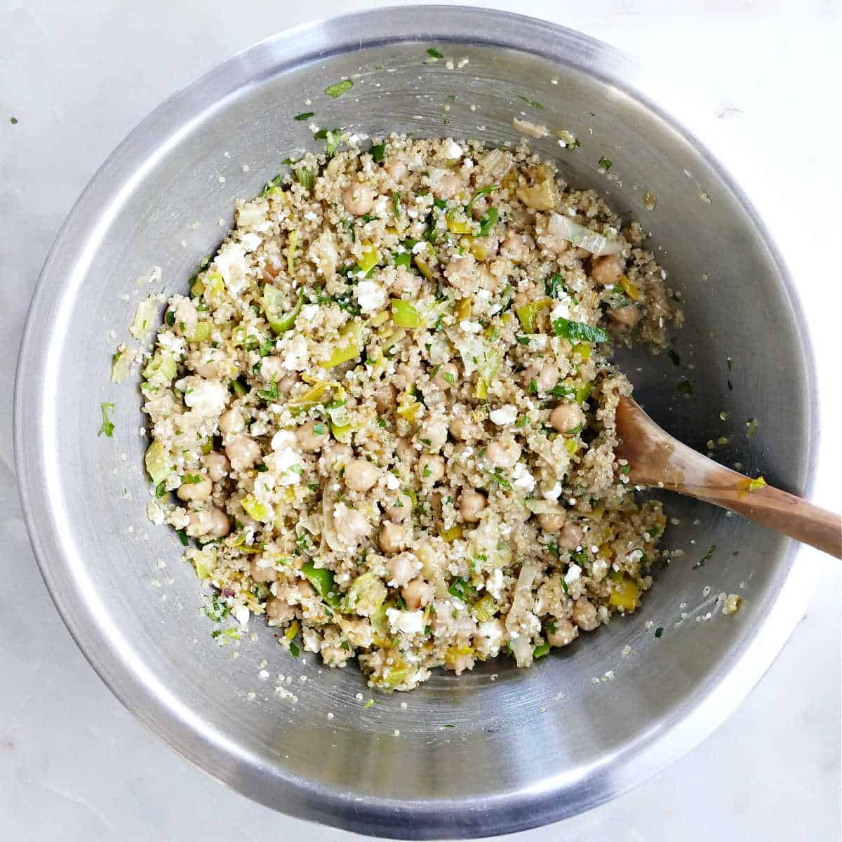 Quinoa leek salad in a stainless steel mixing bowl with a wooden spoon.