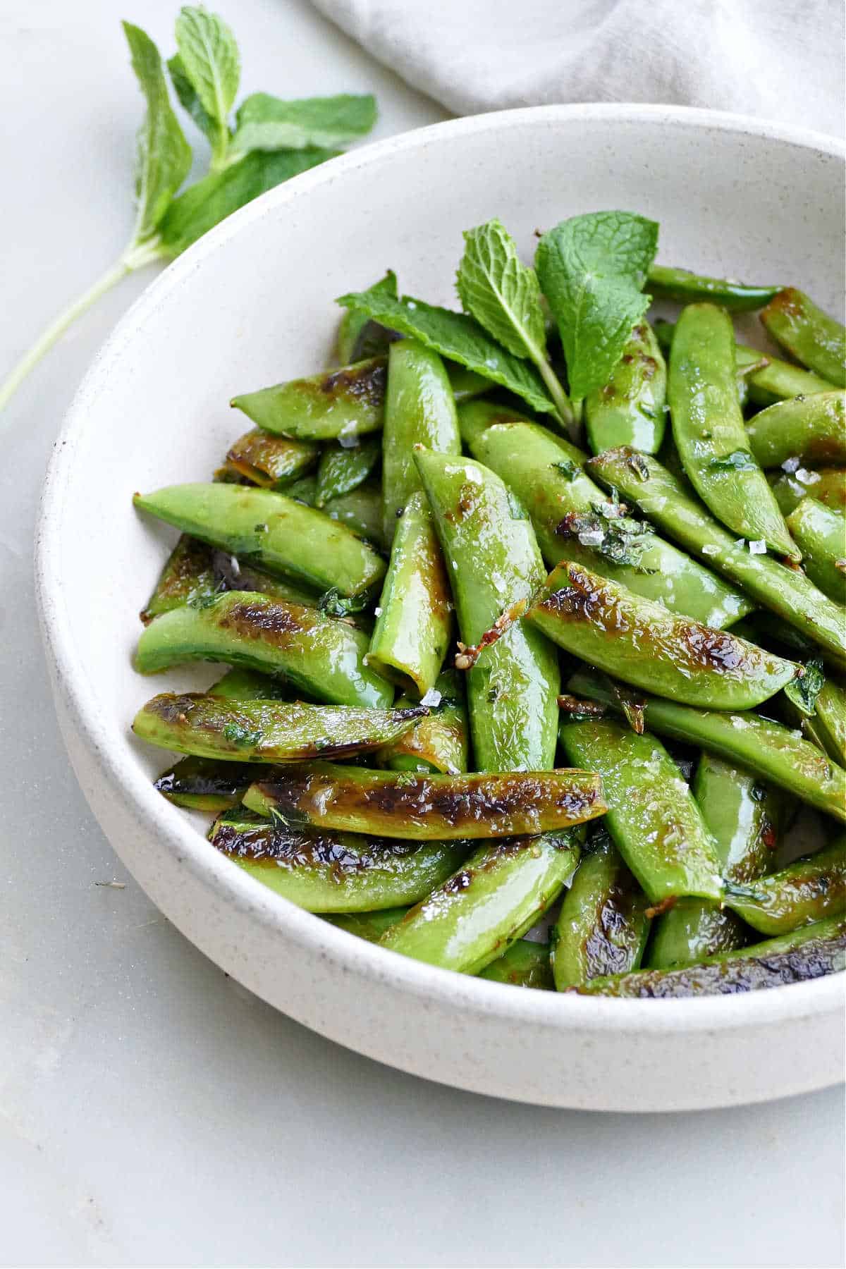 Sauteed snap peas in a white serving bowl.