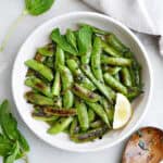 Blistered snap peas in a large serving bowl with a lemon slice.
