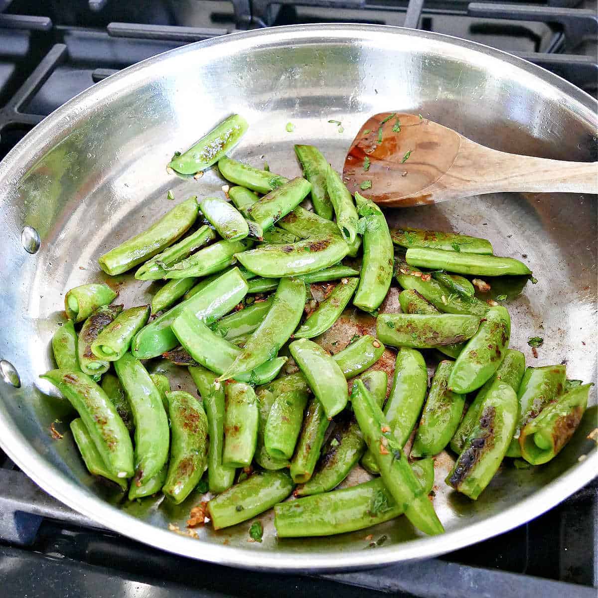 Sauteeing snap peas in a large skillet with a wooden spoon.