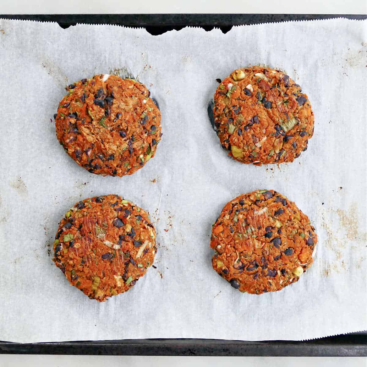 Four sweet potato black bean burgers on a parchment lined sheet pan after baking.