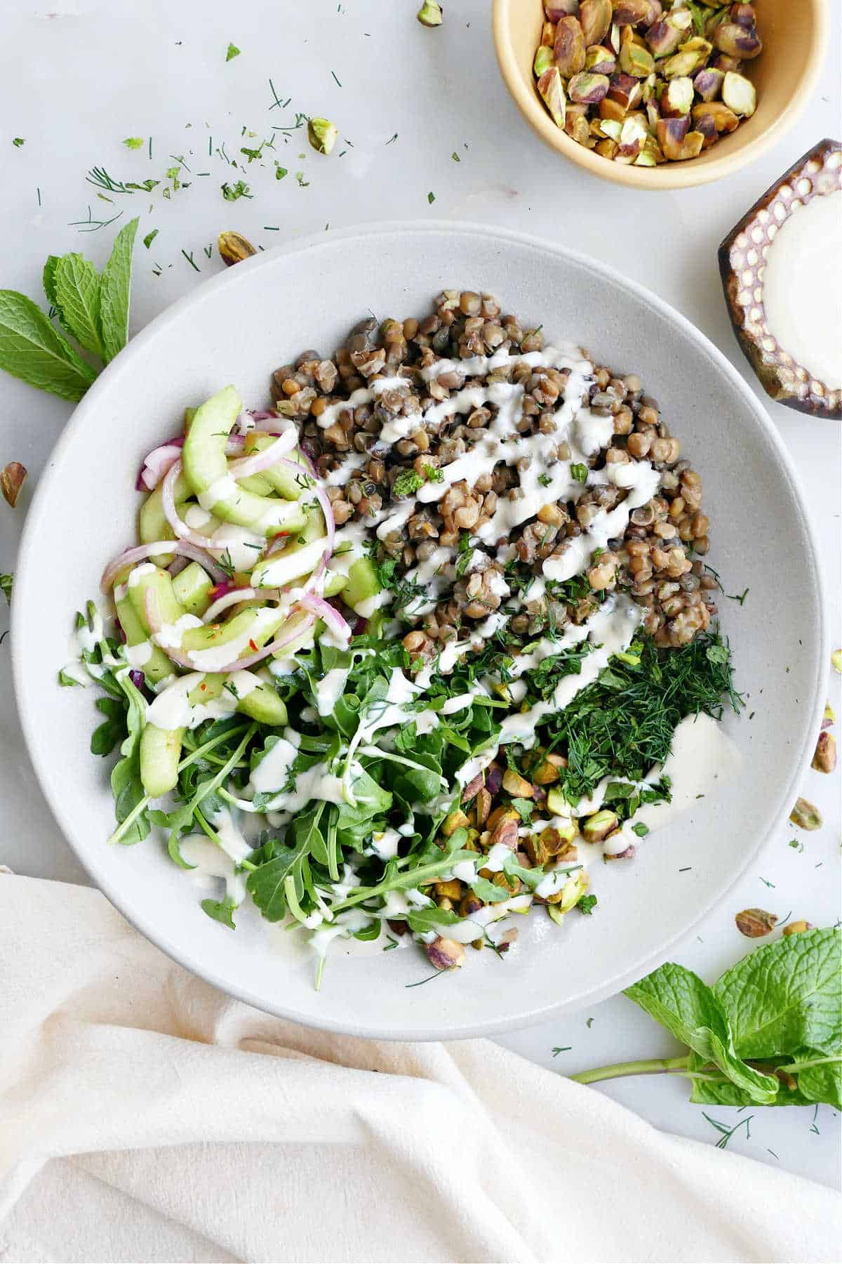 Lentil bowl with vegetables next to a ramekin of pistachios.