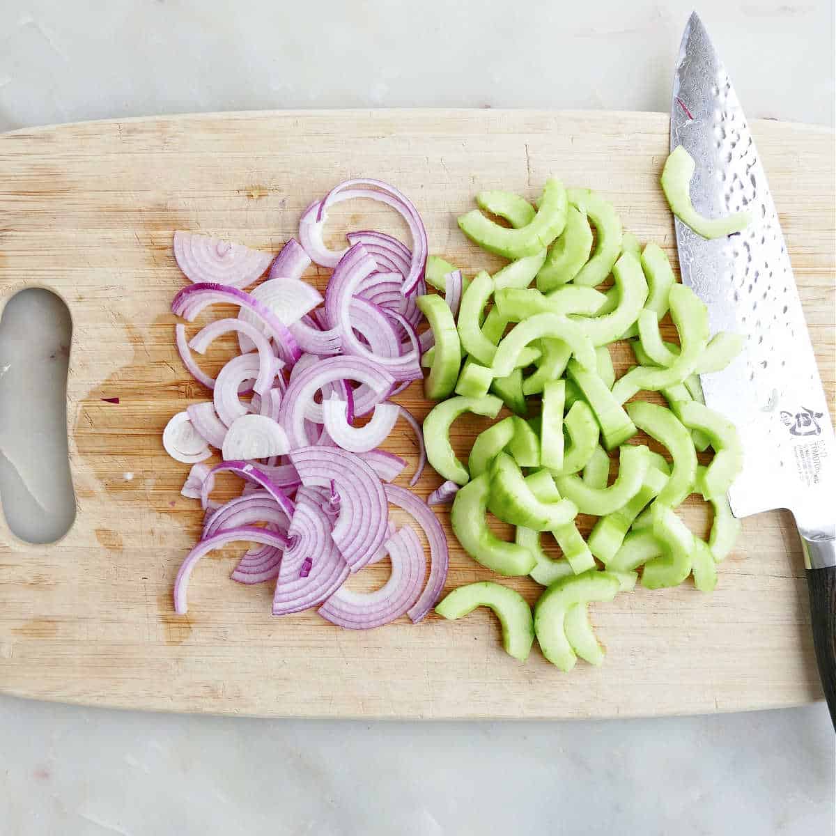 Chopped onions and cucumbers on a cutting board with a knife.