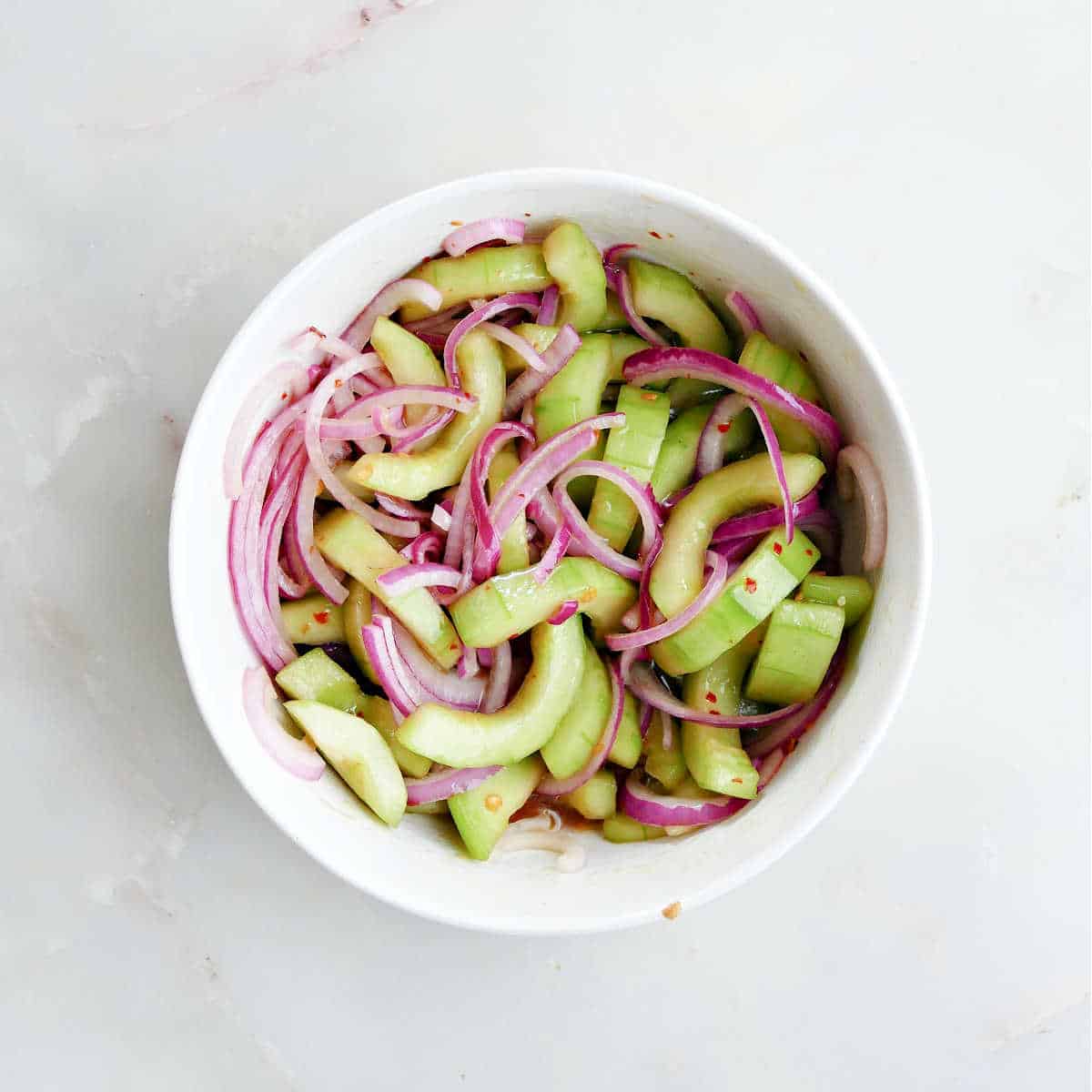 Marinating the cucumbers and onions in a small white bowl.