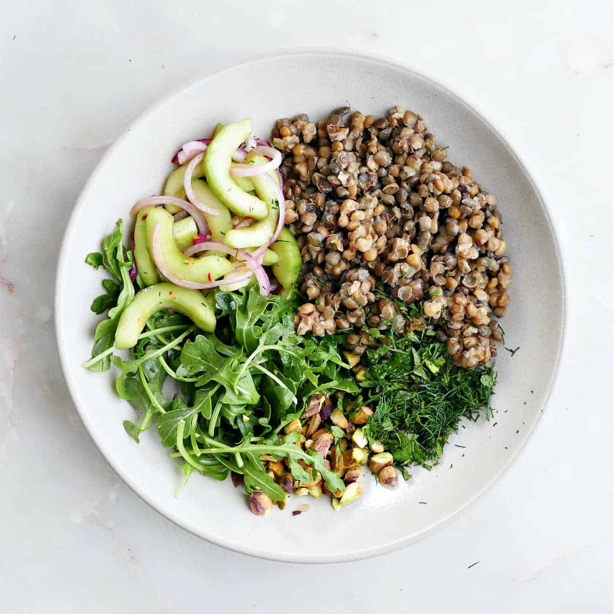 Veggies, lentils, herbs, and arugula in a large white bowl.