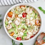 A bowl of shrimp orzo salad topped with garnish next to a wooden spoon.