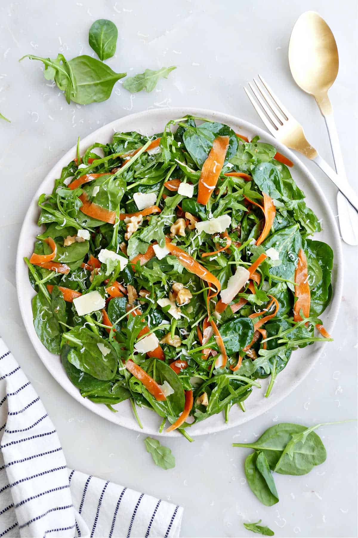 A large spinach arugula salad next to a kitchen towel, fork, and spoon.