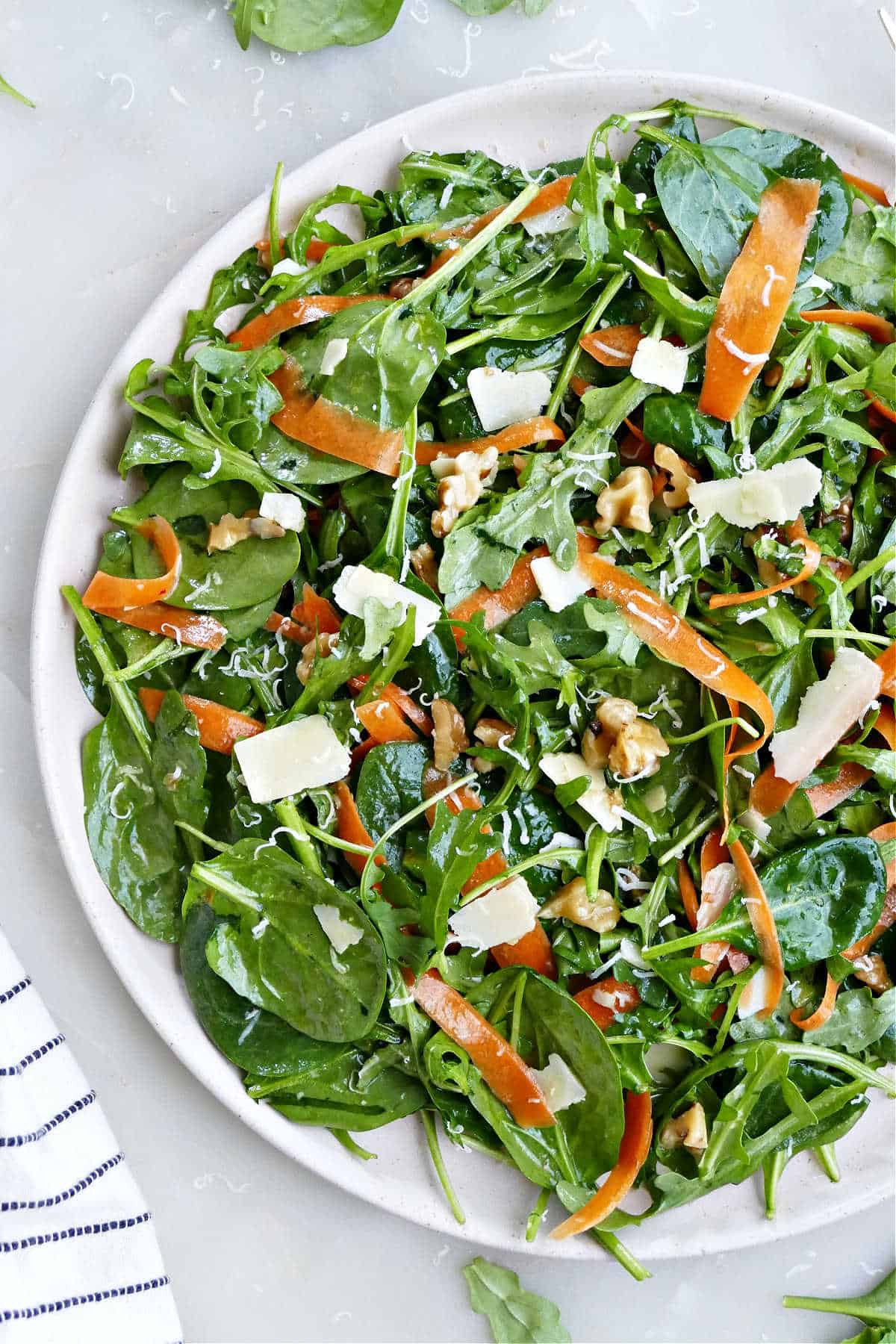 Spinach arugula salad on a plate with parmesan cheese, carrots, and tossed in a homemade dressing.