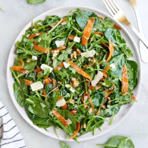 Spinach arugula salad on a large white plate tossed in dressing next to a fork.