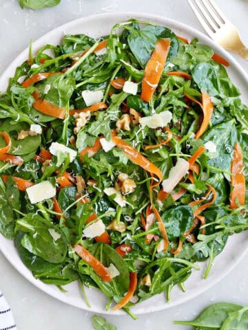 Spinach arugula salad on a large white plate tossed in dressing next to a fork.