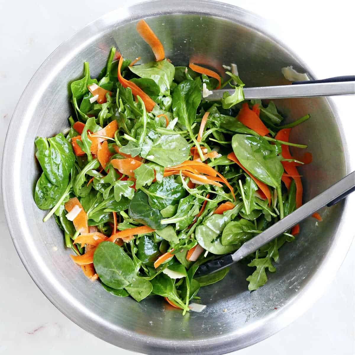 A bowl of spinach arugula salad with carrots.