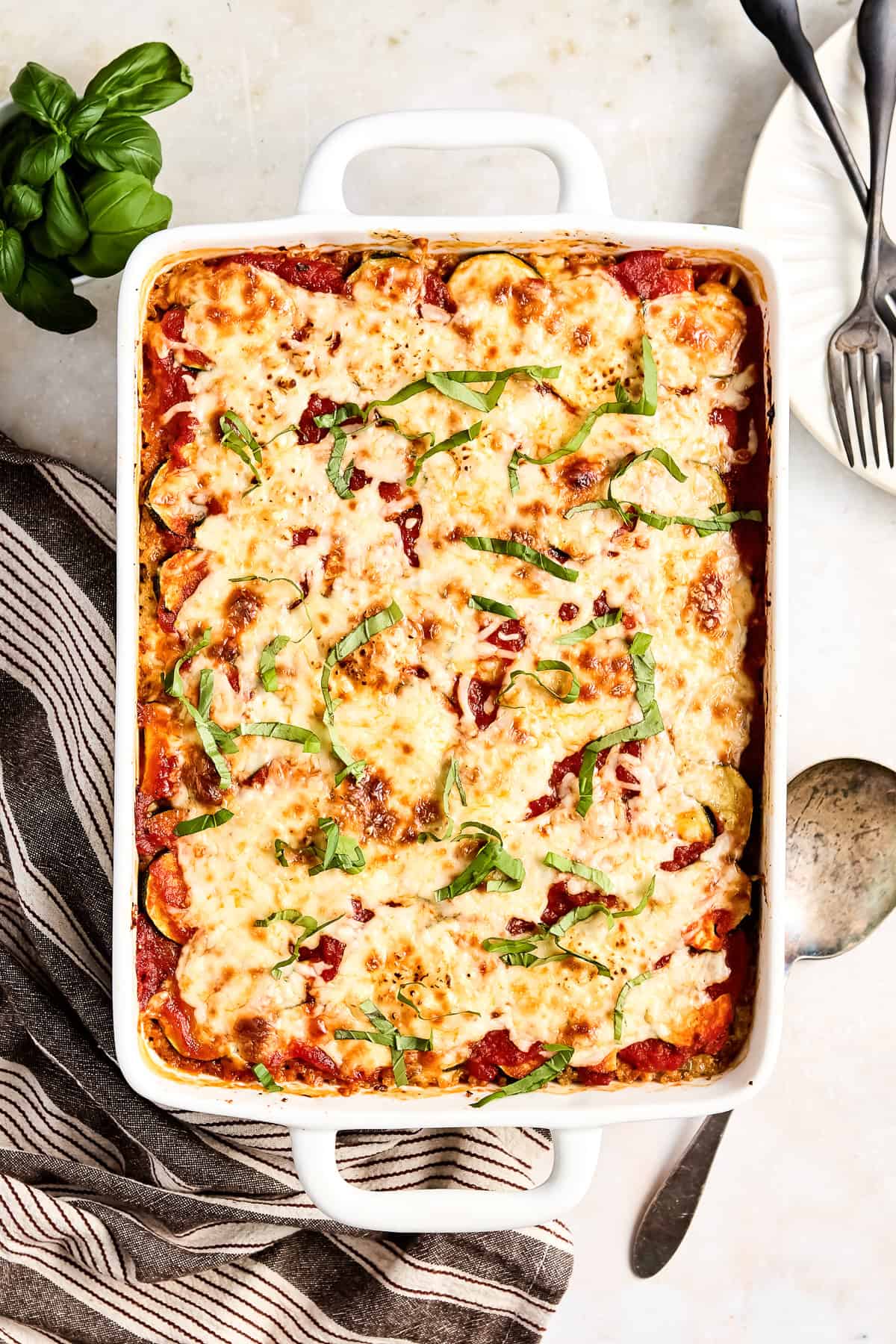 Ground beef zucchini casserole in a baking dish sprinkled with basil next to a napkin.