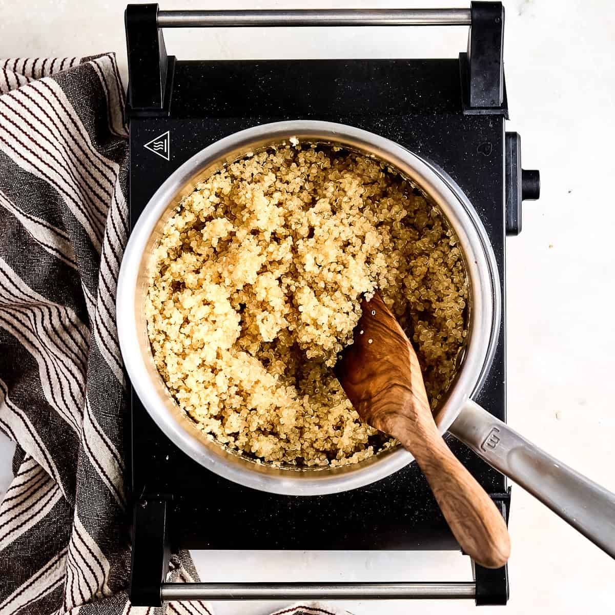 Cooked quinoa in a saucepan with a wooden spoon on a hot plate.