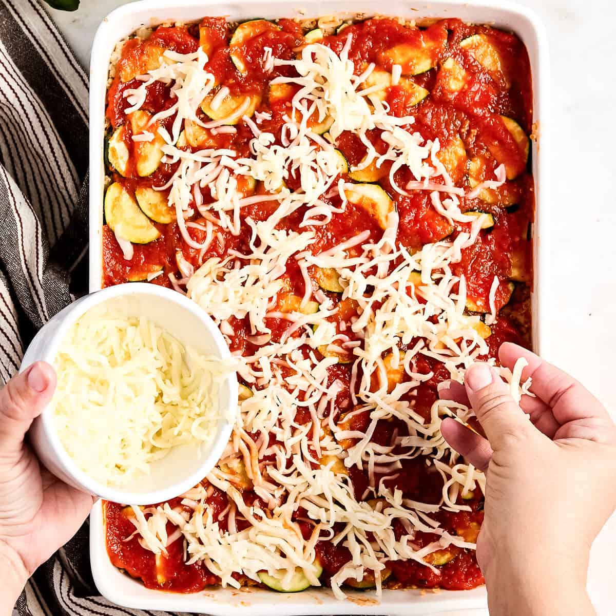 Woman sprinkling mozzarella cheese on zucchini ground beef casserole in a dish.