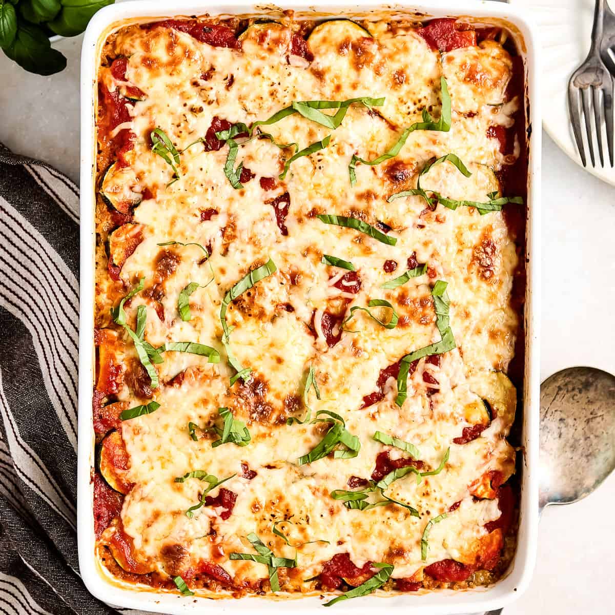 Ground beef zucchini casserole in a baking dish sprinkled with basil next to a napkin.