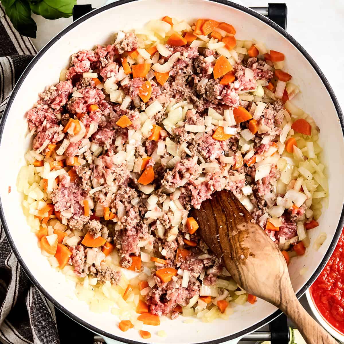 Woman breaking up ground beef in a skillet with veggies cooking.