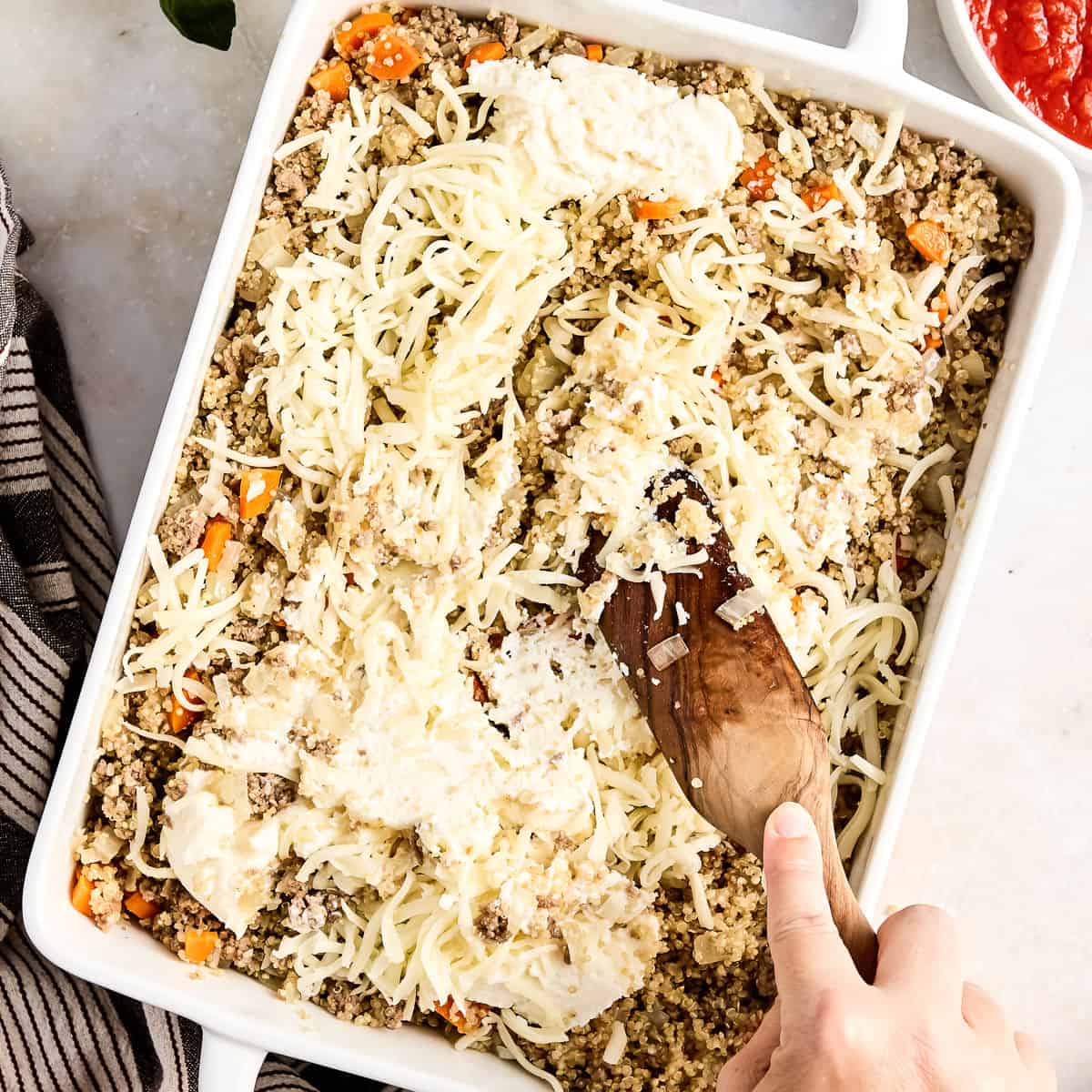 Woman stirring ricotta and mozzarella cheese into ground beef and veggie mixture in a dish.