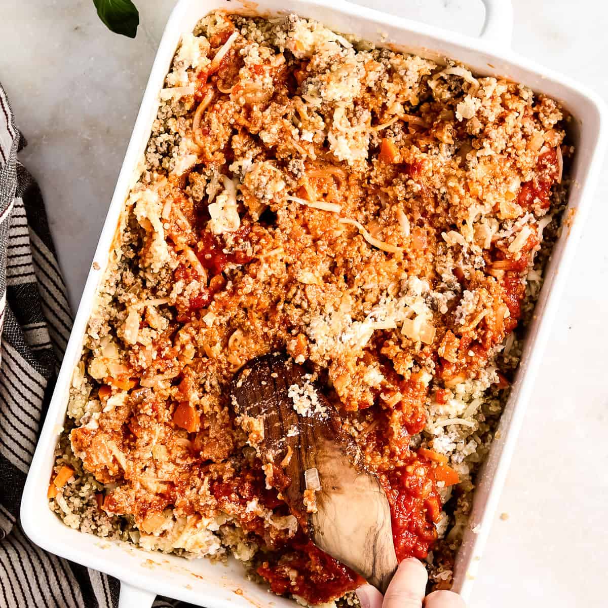 Woman mixing ground beef zucchini casserole filling together with a spoon in a dish.