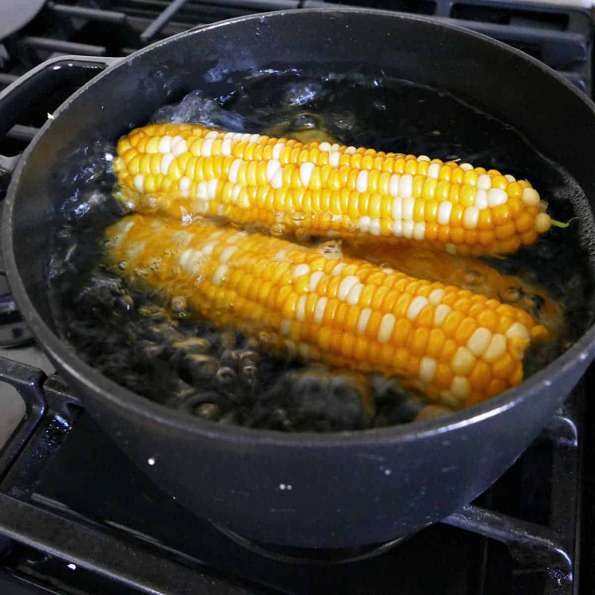 Corn on the cob cooking in a pot of boiling water on the stove.