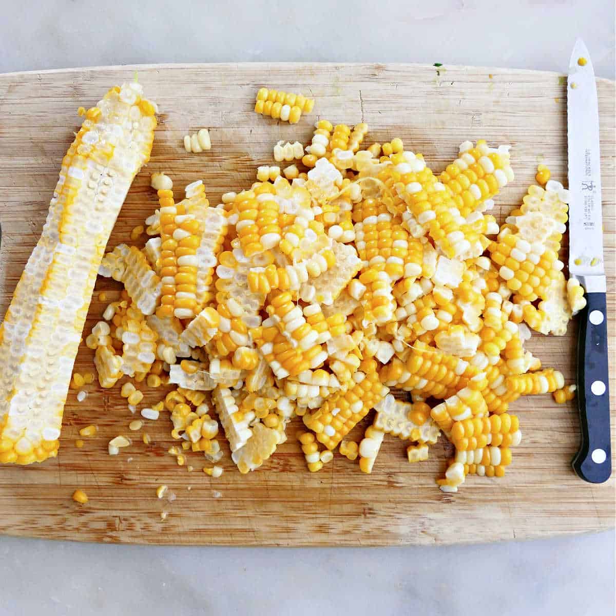 Corn kernels on a cutting board after being cut off the cob with a serrated knife.