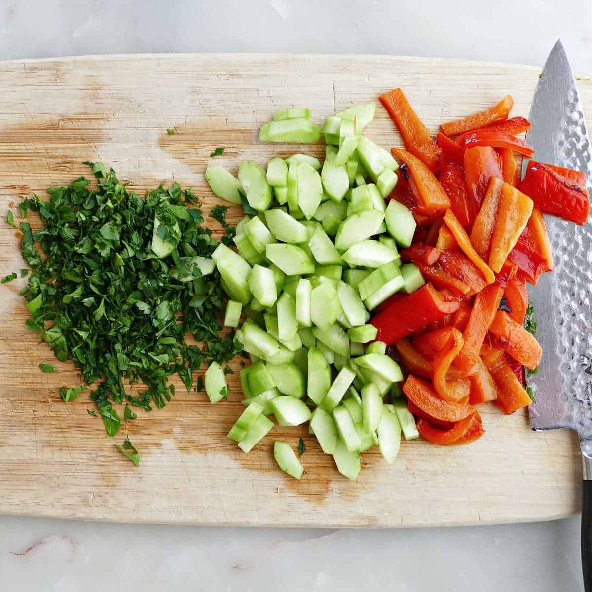 Chopped veggies on a cutting board with a knife for cold Italian farro salad.