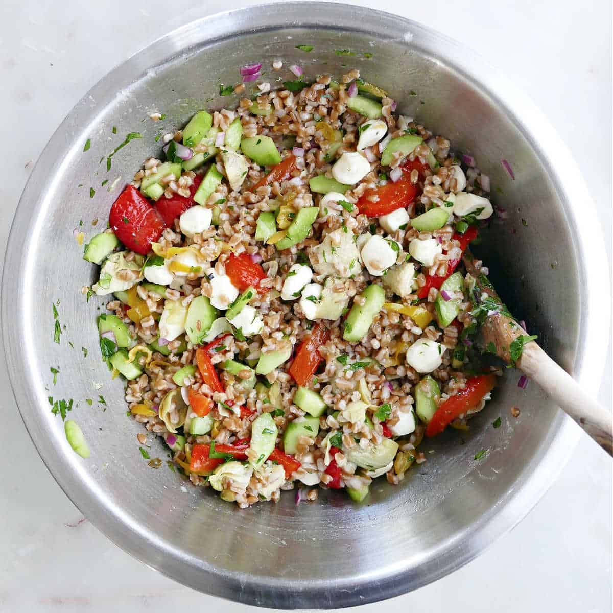 Mixing together the cold Italian farro salad in a stainless steel bowl with a wooden spoon.